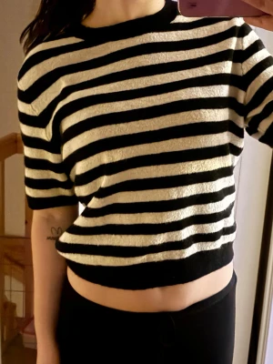 Svartvit randig croppad topp - Säljer en croppad topp med breda svarta och vita horisontella ränder. Toppen har korta ärmar, rund halsringning och är gjord i ett mjukt, lite strukturerat material. Perfekt för en avslappnad och trendig look.