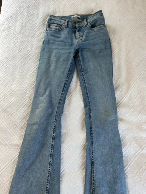 Ljusblå bootcut jeans - Snygga ljusblå bootcut jeans med klassisk femficksdesign och låg midja. Jeansen har en lätt tvättad look och är tillverkade i denim med lite stretch för skön passform. Perfekta till en avslappnad stil.