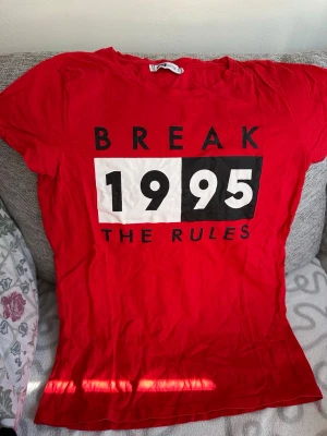 Röd t-shirt med tryck från FB Sister storlek: S - Cool röd t-shirt från FB Sister med stort tryck på framsidan där det står 'BREAK 1995 THE RULES' i svart och vitt. Klassisk rund hals och korta ärmar. Perfekt för dig som gillar statement-plagg och vill sticka ut lite extra.