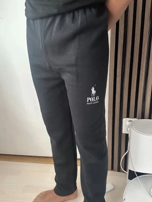 Svarta mjukisbyxor Polo Ralph Lauren - utan etiketter och fickor!!!Säljer ett par svarta mjukisbyxor från Polo Ralph Lauren med vit logga på vänster lår. Byxorna har resår i midjan och är raka i modellen. Perfekta för chill dagar hemma eller när du vill ha en avslappnad stil.