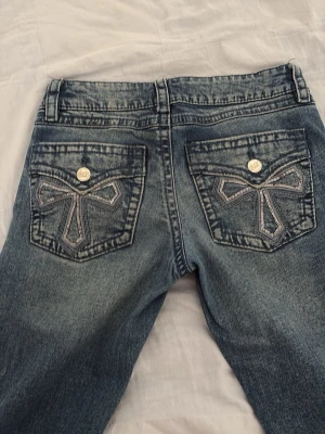 Blå jeans med broderade bakfickor - Medel blå flared/bootcut jeans med coola broderade mönster på bakfickorna med paljetter från Gina tricot. Jeansen är använda men i mycket bra skick.