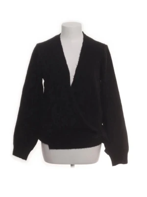 Svart stickad omlott-tröja - Svart stickad tröja med omlott-skärning och djup v-ringning. Tröjan har långa ärmar och ribbade muddar vid ärmslut och nederkant. 