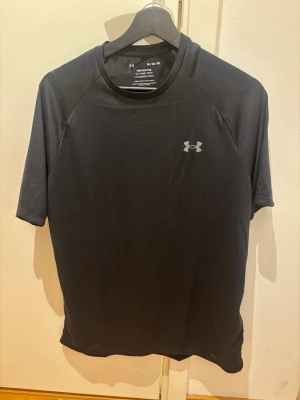 Svart tränings-tshirt från Under Armour - Svart tech-tshirt från Under Armour med korta ärmar och rund hals. Tillverkad i ett lätt och snabbtorkande material som passar perfekt för träning. Diskret logga på bröstet. Modellen är lös och bekväm för rörelsefrihet.