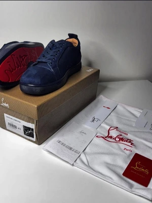 Marinblå sneakers Christian Louboutin - Snygga marinblå sneakers från Christian Louboutin i mocka med klassisk röd sula och diskret logga. Skorna har rund tå, matchande snörning och en stilren design som passar till det mesta. Kommer med originalkartong och dustbag.