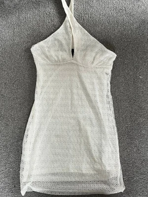 Vit spetsklänning från H&M Divided - Snygg vit kort klänning från H&M Divided med halterneck och spetsdetaljer samt öppen rygg. Har aldrig använt