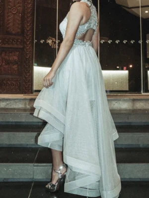 Vit långklänning med öppen rygg - Elegant vit långklänning med asymmetrisk fåll och öppen rygg. Klänningen har broderade detaljer upptill, markerad midja och är ärmlös. Perfekt för speciella tillfällen där du vill sticka ut med en unik och stilren look.