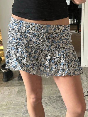 Zara Skort - Supersöt kort kjol med inbyggda shorts. Kjolen har volangdetaljer och snörning i midjan för extra stilpoäng. Perfekt för dig som vill ha en lekfull och trendig look.