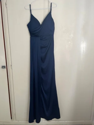 Navy balklänning med omlott - Navy Aftonklänning/balklänning/brudtärneklänning/maxiklänning från Eva & Lola Paris  Helt ny och oanvänd med prislapp.  Färg: navy/mörkblå. Det finns insydda kupor i bysten. Slits. Dragkedja i ryggen för att stänga klänningen. Satinliknande material. Passar mig perfekt som är cirka 170, ger släp vid fötterna.  Mått:  - Byst: cirka 80cm - Midja: cirka 65-70cm - Längd från armhålan och ner: cirka 140 cm 