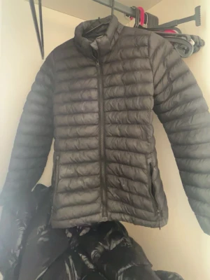 Svart lättviktsdunjacka - Säljer en svart lättviktsdunjacka med quiltad design och dragkedja framtill. Jackan har hög krage och två sidofickor med dragkedja. Perfekt för kalla vinterdagar och enkel att matcha till olika outfits.