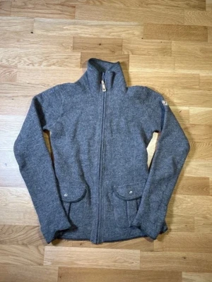 Fjällräven Wool zip - Fjällräven ulljacka med dragkedja i storlek S. Ett varmt och slitstarkt plagg, perfekt för utomhusaktiviteter eller vardagsbruk i svalare väder.  Högkvalitativt ullmaterial med praktisk dragkedja. Lätt att bära över skjortor eller tröjor för en bekväm och funktionell look.  Modell: Kyla tröja Om du har några frågor om bilder eller mått, tveka inte att kontakta mig.  