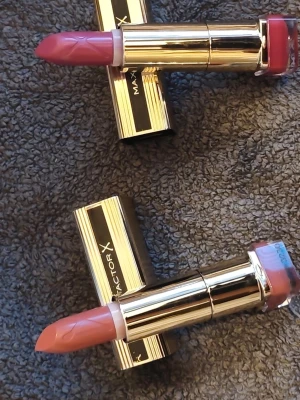 Max Factor X läppstift duo - Två stilrena läppstift från Max Factor X med lyxiga guldfärgade hylsor. Ena stiftet har en mjuk rosa nyans och det andra en varm nude-ton. Klassisk form på stiften och smidiga att applicera. Perfekta för dig som vill ha både färg och vård till läpparna.