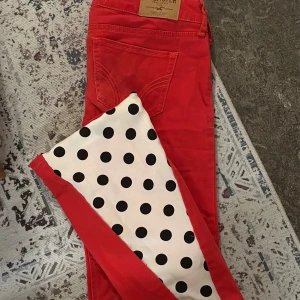 Röda prickiga  jeans från Hollister - Snygga röda jeans från Hollister med klassisk femficksmodell och normal midja. Jeansen har raka ben och är tillverkade i ett mjukt bomullsmaterial med lite stretch för extra komfort. Perfekta för dig som vill sticka ut med färg i din outfit. Storlek 27, passar mig som bär xs/s. Sydda bootcut