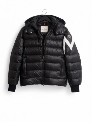 Svart dunjacka från Moncler - Kvitto finns!!!!!! Snygg svart dunjacka från Moncler med huva och dragkedja. Jackan har ett vitt M-format mönster på ena ärmen och Moncler-logga. Puffig modell med ribbade muddar och två fickor framtill. Perfekt för kalla vinterdagar.