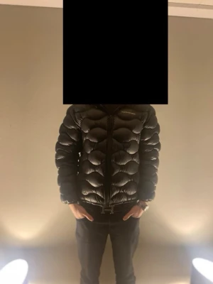 Svart dunjacka från Peak Performance - Snygg svart dunjacka från Peak Performance med unik quiltad design och dragkedja framtill. Jackan är lätt och smidig, perfekt för kalla vinterdagar. Klassisk passform och diskret logga på bröstet. Passar dig som vill ha både stil och värme.