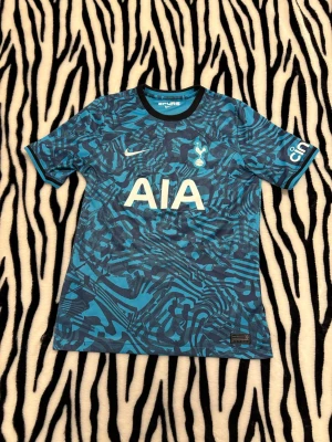 Tottenham Hotspur tröja - Snygg blå och turkos Tottenham Hotspur från Nike med grafiskt mönster, klubbmärke och sponsortryck på bröstet. Nummer 10 och namnet Kane på ryggen. Perfekt för fotbollsfans som vill sticka ut på läktaren eller planen. Inte använd mycket så bra skick! Barn storlek 👍 hör av dig vid minsta fundering 