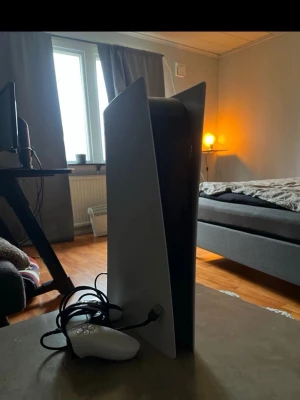 PlayStation 5 konsol med handkontroll - Säljer en PlayStation 5 konsol från Sony i vit och svart design. Konsolen har en futuristisk form med vita sidopaneler och svart mitt. Medföljer en vit handkontroll med USB-kabel. Perfekt för gaming och nästa generations spelupplevelser. 1 kontroll ingår