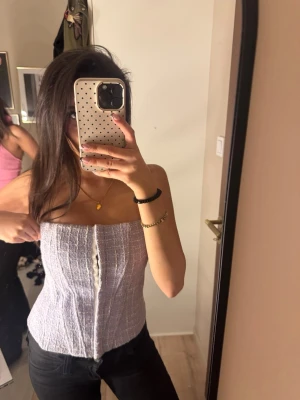 Ljuslila korsett-topp - Trendig ljuslila korsett-topp med knappar framtill. Toppen är axelbandslös och har en figurnära passform som framhäver midjan. Materialet är strukturerat och ger en snygg look. Perfekt att styla med jeans eller kjol.