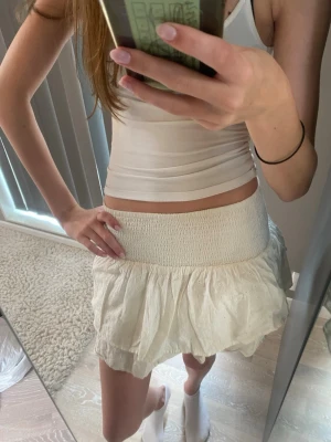 Vit volangkjol med bred resår - Supersöt vit kortkjol med bred smockresår i midjan och volangig nederdel. Kjolen är gjord i ett lätt bomullstyg med små blommiga hål-mönster. Perfekt för sommarens alla outfits!💓☀️