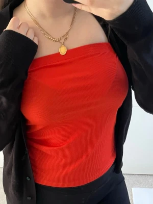 Röd ribbad bandeau tubtopp - Trendig röd bandeau tubtopp med ribbad struktur. Toppen är axelbandslös och har en croppad passform som sitter snyggt på kroppen. Perfekt att styla med jeans eller kjol för en cool look. Storleken är L men passar en XS/S/.