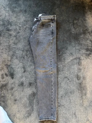 Grå slim jeans från Calvin Klein - Snygga grå skinny jeans från Calvin Klein med klassisk femficksdesign och svart logotyppatch bak i midjan. Jeansen har smal passform och är tillverkade i stretchigt denim för en bekväm känsla. Perfekta för en trendig och avslappnad stil.