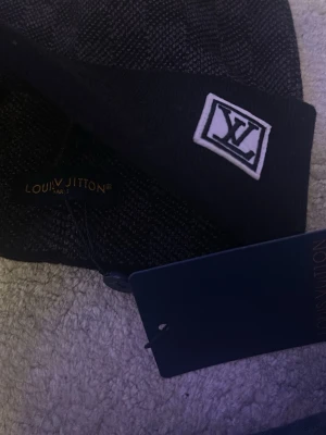 Stilren Svart/Grå Designer Mössa – Ny med Tags - Säljer en stilren svart och grå mössa med klassisk design och diskret logodetalj framtill. Mössan har en modern passform och är tillverkad i mjukt och bekvämt material som håller värmen bra under kallare dagar.  Den passar perfekt både till vardags och till en mer uppklädd streetwear-stil. Mössan är helt ny och kommer med tags kvar.  Detaljer: • Färg: Svart / Grå • Stilren logodetalj framtill • Ny med tags • Bekväm och varm passform  Perfekt för dig som vill ha en snygg och stilren mössa till hö