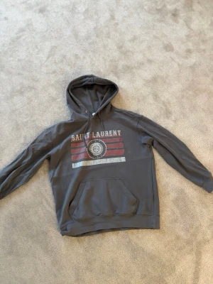 Saint Laurent hoodie  - Saint Laurent hoodie i mycket fint skick. Stilren och eftertraktad modell som passar perfekt till både vardag och streetwear. Hoodien har en premiumkänsla och bra passform.  Använd få gånger och fortfarande i väldigt bra skick. Perfekt om du vill ha ett exklusivt plagg från Saint Laurent till ett bättre pris.  Storlek: L ( sitter som M) Färg:  grå  Kvitto ingår såklart. Självklart äkta. Skriv om du vill se kvittot 