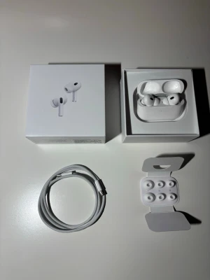 Apple AirPods Pro med laddningsetui - Säljer ett par vita Apple AirPods Pro med trådlöst laddningsetui. Hörlurarna har en stilren och kompakt design i blank plast, silikonproppar i olika storlekar och medföljande USB-C laddkabel. Grym ljudkvalitet och brusreducering.