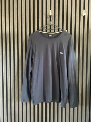 Svart långärmad topp från BOSS - En stilren svart långärmad topp från BOSS med rund halsringning och diskret logga på bröstet. Tillverkad i mjuk bomull för en bekväm känsla. Perfekt till jeans 