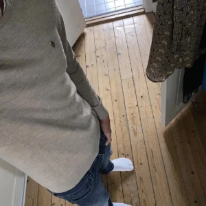 Beige merinoulltröja från Morris - Säljer en stilren beige tröja från Morris i 100% merinoull. Tröjan har rund halsringning, diskret logga på bröstet och ribbade muddar vid ärmslut och nederkant. Perfekt för dig som gillar klassisk och enkel stil.