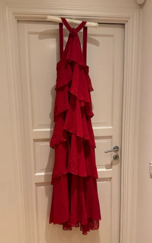 Röd volangklänning från Vero Moda - Klänning från Vero Moda i röd färg med flera lager volanger och smala axelband. Klänningen är ärmlös och har en luftig, flowy för dess tunna polyestertyget. Snyggt för balen eller andra fester! Helt ny med prislappen kvar. Nypris 1200kr! Pris kan diskuteras. 