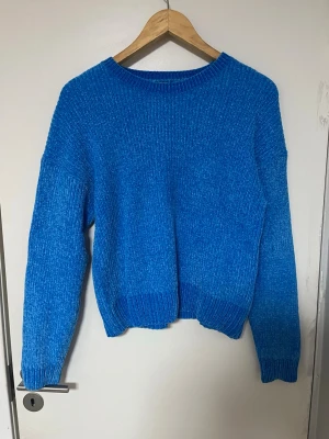 Blå stickad tröja med rund hals - En enkel och snygg blå stickad tröja med rund halsringning och långa ärmar. Tröjan har ribbade muddar vid ärmslut och nederkant, vilket ger en skön passform. Perfekt för att hålla värmen under kyliga dagar.