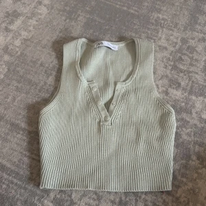 Ribbad ärmlös topp från Zara - Snygg ljusgrön ribbad topp från Zara med knappar framtill. Modellen är ärmlös och croppad, perfekt till jeans eller kjol. Materialet är mjukt och stretchigt, vilket gör den superbekväm att bära.