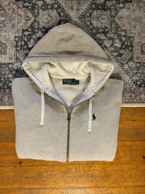 Ljusgrå Ralph Lauren Zip Up Hoodie - Hej!👋  Säljer en väldigt snygg ljusgrå zip up Hoodie från Polo Ralph Lauren. Hoodien har en mycket liten fläck på vänstra ärmen, (se sista bilden). Osäker om fläcken går bort med något bra fläckborttagningsmedel. Fläcken påverkar knappt hoodiens utseende och jag har aldrig riktigt lagt märke till den. Utöver detta så är den i utmärkt skick. Storlek: M Skickar snabbt🚛📦 Hör av er vid frågor!💯