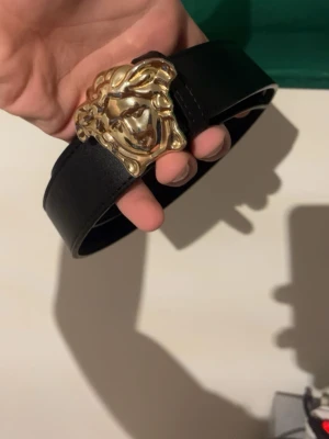 Svart bälte med lejonspänne i guld - Snyggt svart bälte med ett stort guldfärgat lejonspänne som verkligen sticker ut. Bältet är i skinn och har flera hål för justering. Perfekt accessoar för att lyfta vilken outfit som helst.