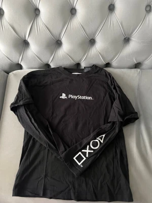 Svart långärmad PlayStation t-shirt ZARA - Säljer en svart långärmad t-shirt ZARA med PlayStation logga tryckt på bröstet och de klassiska PlayStation-symbolerna på ena ärmen. Tillverkad i mjuk bomull och har en normal passform. Storlek 11-12 år eller 152 cm