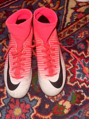 Nike rosa fotbollsskor med strumpa - Säljer ett par snygga fotbollsskor från Nike i rosa och vitt med svarta detaljer. Skorna har en hög strumpa för extra stöd runt ankeln. Skorna är storlek 38. 