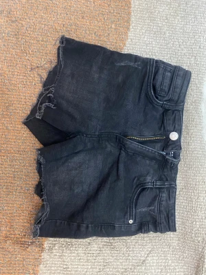 LAB industries Svarta denimshorts med rå kant - Säljer ett par svarta denimshorts från Labl med hög midja och råa, fransiga kanter. Shortsen har klassisk femficksdesign, dragkedja och knapp framtill. Perfekta för sommaren och ger en avslappnad vibe till din outfit. För fler bilder fråga!