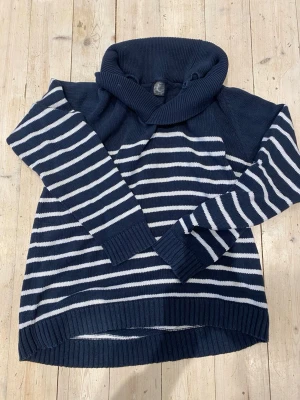 Marinblå randig polotröja Esprit - Stickad marinblå tröja från Esprit med vita horisontella ränder och bred polokrage. Tröjan har långa ärmar och ribbade muddar vid ärmslut och nederkant. Perfekt för kalla dagar och ger en klassisk, avslappnad look.