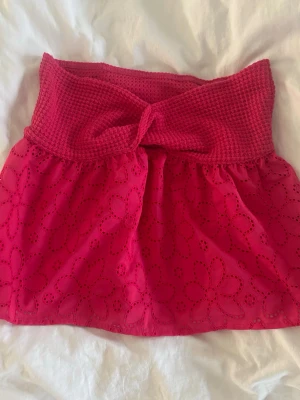 Rosa tubtopp - Söt rosa topp med bred virkad kant upptill och knyt framtill. Nedre delen är i ett blommigt broderat tyg som ger en luftig känsla. Perfekt för varma dagar och somriga outfits. Aldrig använd.