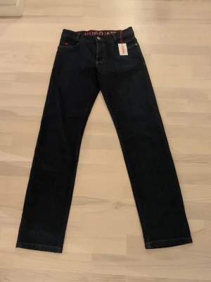 Hugo blå Jeans  - Säljes ett par blåa jeans i märke Hugo 677 som är helt oanvända med prislappen kvar. Modellen är regular straight och passar på barn mellan 13-14år storlek 164. Här finns jeansen nypris hos kidsbrandstore: https://kidsbrandstore.se/products/denim-trousers-669717?utm_source=bing&utm_medium=cpc&utm_campaign=p-se-shopping-main-new&msclkid=7c3fe1c572fe14dafaef8804b90eaa62&utm_term=4587231241408486&utm_content=sale