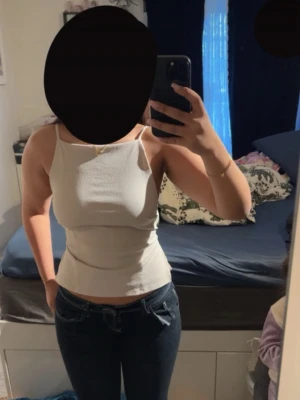 Vit ribbad linnetopp med öppen rygg - Säljer en vit ribbad linnetopp med smala axelband och öppen rygg med snygga banddetaljer. Toppen är croppad och har en figurnära passform som passar perfekt till jeans eller kjol. Superenkel att styla för en trendig look.