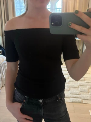 Svart offshoulder ribbad topp - Säljer en svart ribbad offshoulder topp med korta ärmar. Toppen har en tight passform och är perfekt för dig som gillar en enkel men snygg stil. Materialet känns mjukt och stretchigt, vilket gör den bekväm att bära.