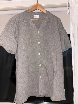2 linneskjortor kort ärm herr - Två snygga linneskjortor med kort ärm. Ena skjortan är grå och stilren, den andra är beige från Lindbergh med vitt blommigt och palmigt mönster. Båda har knappar framtill och avslappnad passform, perfekta för sommaren. Storlek XXL. Båda för 350kr eller en för 200kr