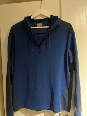 Blå hoodie från Callaway - Snygg blå hoodie från Callaway med dragkedja framtill och justerbar huva. Tröjan har långa ärmar och är gjord i ett mjukt material som känns skönt mot huden. Färgblock i olika blå nyanser ger en sportig look. Perfekt för dig som gillar en avslappnad stil. Perfekt på kalla sommardagar. Har aldrig använt denna tröja