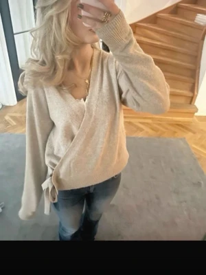 Beige omlottkofta med knytband - Mysig beige omlottkofta med knytband i sidan och ribbade muddar. Koftan har en avslappnad passform och långa ärmar, perfekt att slänga över en topp. Passar till jeans eller kjol för en chill look.