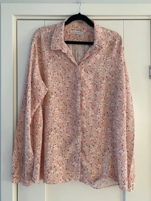 Blommig rosa blus från The Shirt Factory  - Söt blommig blus från The Shirt Factory i ljusrosa med vita och svarta blommor. Blusen har klassisk krage, knäppning framtill och långa ärmar. Tunt och luftigt material som ger en avslappnad känsla. The shirt Factory rosa blus med vita blommor strl 44 i viskos  Endast tvättad men aldrig använd  Mått Över bröstet: ca 62 cm Längd från axeln och ner: ca 70 cm  100% viskos  Kommer från ett djur och rökfritt hem 