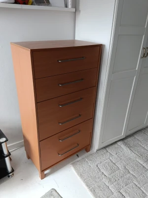 Byrå i trä med sex lådor - Praktisk byrå i ljusbrunt trä med fem stora lådor och långa, stilrena handtag i metall. Perfekt för att organisera kläder, accessoarer eller småprylar. Enkel, modern design som funkar i sovrum, hall eller vardagsrum.