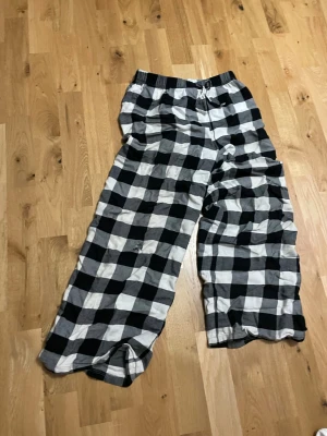 Rutiga pyjamasbyxor från H&M - Säljer ett par svartvita rutiga pyjamasbyxor från H&M i storlek 146/152. Byxorna har resår i midjan med dragsko och är tillverkade i mjukt bomullstyg. Perfekta för mysiga hemmakvällar eller lata morgnar.