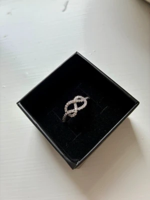 Ring i sterlingsilver med stenar - Ring i sterlingsilver (stämplad, se bild), med stenar. Formad som evighetstecknet, men är snygg i alla sammanhang. Väldigt vackra detaljer i flätningen av metallen. Storlek 18. Nypris 1150kr.  Kan skickas eller hämtas hos mig på Kungsholmstorg.