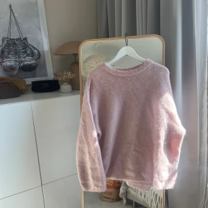 Ljusrosa fluffig stickad tröja  - Mysig ljusrosa stickad tröja med rund hals och långa ärmar. Tröjan har en fluffig, mjuk struktur och ribbade muddar vid hals, ärmslut och nederkant. Perfekt för lager på lager och en avslappnad look. Från HMs premium kollektion